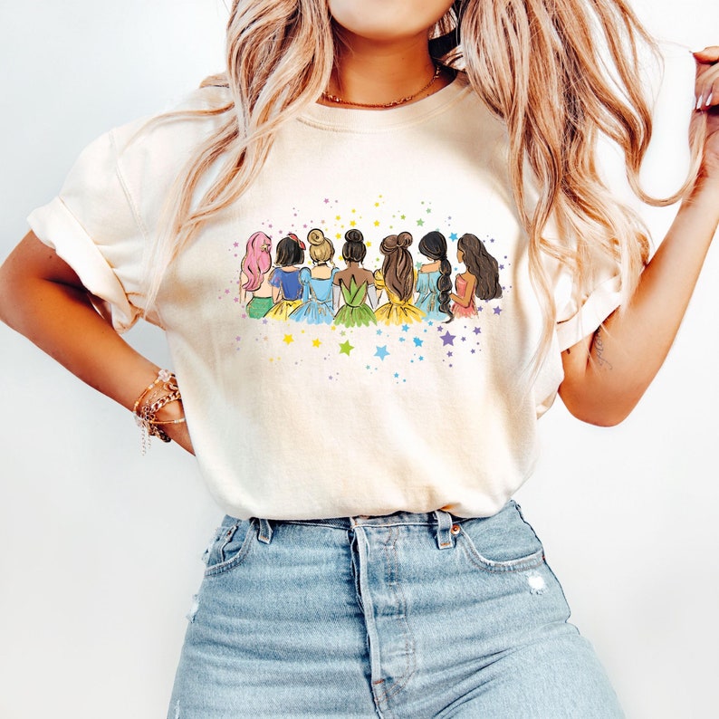 May include: A white t-shirt with a graphic of seven cartoon princesses standing back to back with a rainbow of colors and stars.