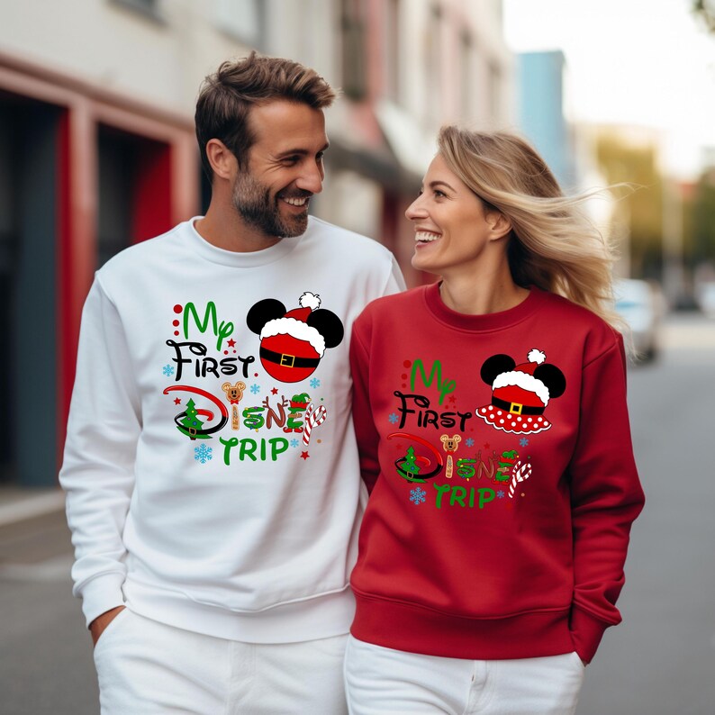 May include: A couple wearing matching white and red Christmas sweaters with the text "My First Disney Trip" and a Mickey Mouse head with a Santa hat. The sweaters feature a Christmas tree, candy canes, and a small Mickey Mouse head.
