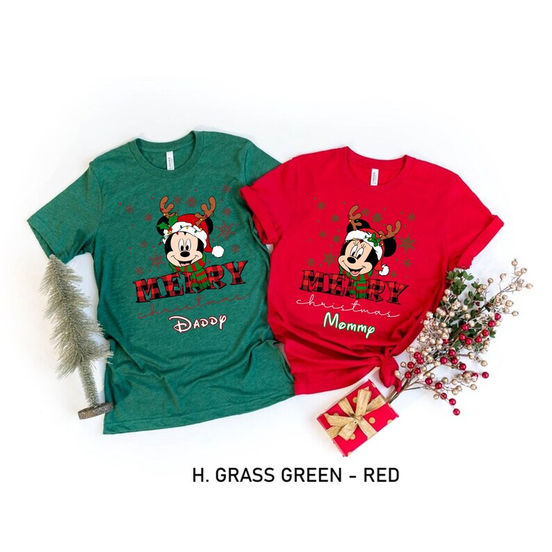 May include: Two Christmas themed t-shirts featuring a cartoon Mickey Mouse wearing a Santa hat and reindeer antlers. The green shirt says "Merry Christmas Daddy" and the red shirt says "Merry Christmas Mommy".