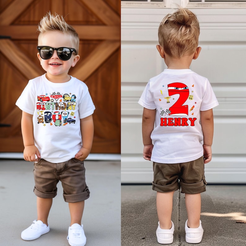 May include: White t-shirt with a Cars birthday boy design on the front and a red number 2 with the name Henry on the back. The shirt is being worn by a young boy wearing brown shorts and white sneakers.