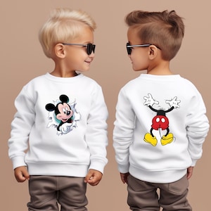 Puede incluir: Sudadera blanca con un dise&ntilde;o de Mickey Mouse. La parte delantera muestra a Mickey rompiendo un efecto rasgado, y la parte trasera muestra todo el cuerpo de Mickey. La sudadera la lleva un ni&ntilde;o.