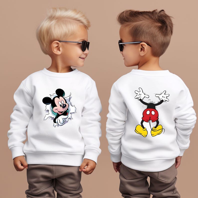Puede incluir: Sudadera blanca con un dise&ntilde;o de Mickey Mouse. La parte delantera muestra a Mickey rompiendo un efecto rasgado, y la parte trasera muestra todo el cuerpo de Mickey. La sudadera la lleva un ni&ntilde;o.