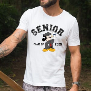Op de afbeelding: Wit T-shirt met een zwart-witte afbeelding van Mickey Mouse die een afstudeerpet en toga draagt en een diploma vasthoudt. De tekst "SENIOR" staat boven Mickey Mouse en "CLASS OF 2025" eronder.