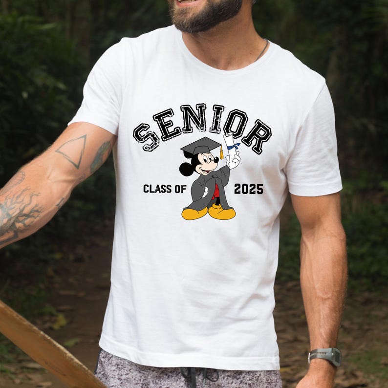 Op de afbeelding: Wit T-shirt met een zwart-witte afbeelding van Mickey Mouse die een afstudeerpet en toga draagt en een diploma vasthoudt. De tekst "SENIOR" staat boven Mickey Mouse en "CLASS OF 2025" eronder.