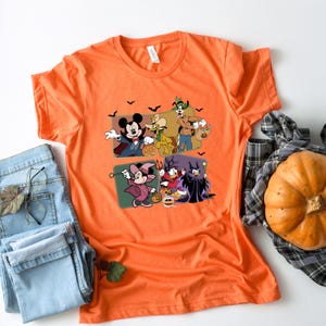 Puede incluir: Camiseta naranja con un dise&ntilde;o de Halloween con personajes de Disney. El dise&ntilde;o incluye Mickey Mouse, Minnie Mouse, Donald Duck y Goofy con disfraces, junto con murci&eacute;lagos y calabazas. La camiseta est&aacute; hecha de un material suave.