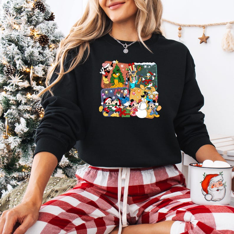 May include: Black crew neck sweatshirt featuring a colorful graphic of Disney characters celebrating Christmas. The graphic includes Mickey Mouse, Minnie Mouse, Donald Duck, and Goofy in festive scenes. The sweatshirt is paired with red and white plaid pajama pants.