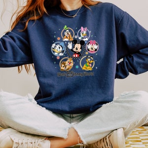 Op de afbeelding: Een donkerblauw sweatshirt met een afbeelding van Mickey Mouse en andere Disney-figuren in een cirkel om hem heen. De tekst "Walt Disney World" staat onder de afbeelding.