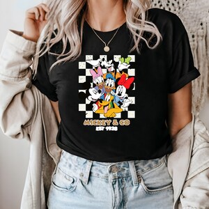 Puede incluir: Camiseta negra con un fondo a cuadros con Mickey Mouse y sus amigos. El texto "Mickey & Co. Est 1928" est&aacute; impreso debajo de la imagen.