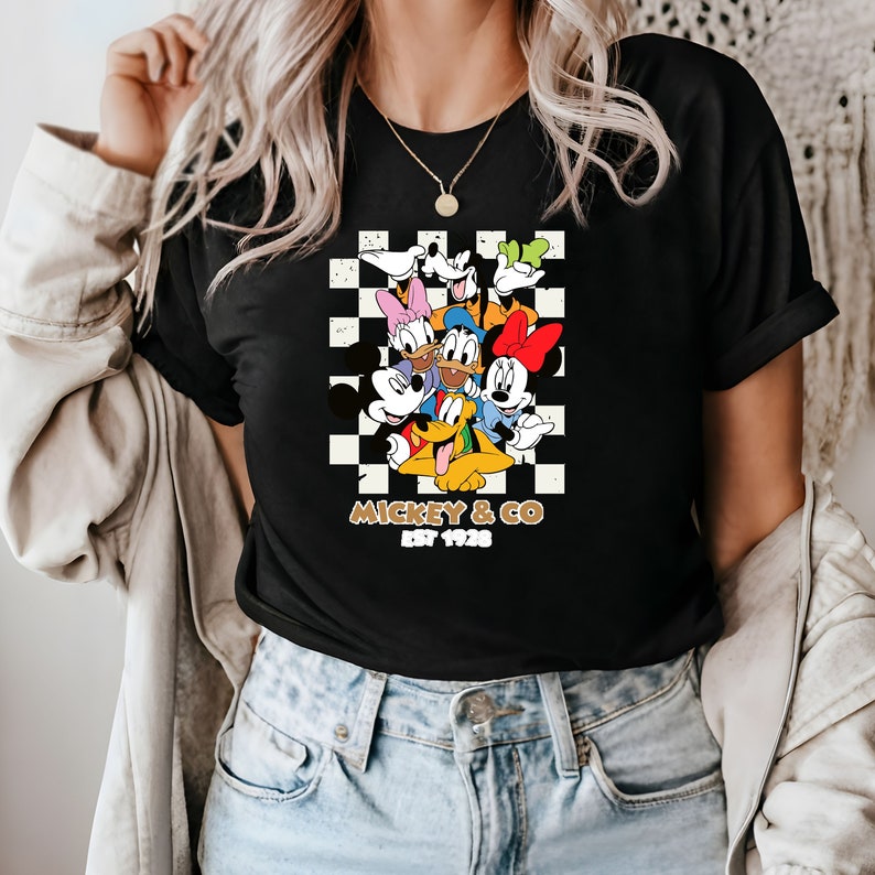 Puede incluir: Camiseta negra con un fondo a cuadros con Mickey Mouse y sus amigos. El texto "Mickey & Co. Est 1928" est&aacute; impreso debajo de la imagen.