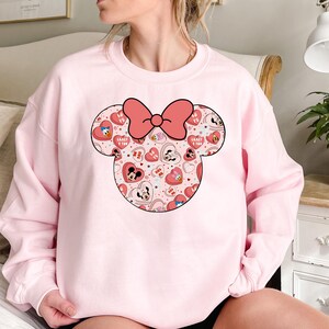 May include: Pink sweatshirt with a large graphic of Mickey Mouse ears with a bow. The ears are filled with a pattern of hearts, Mickey Mouse characters, and the words "Crazy 4 You" and "Love Ya".