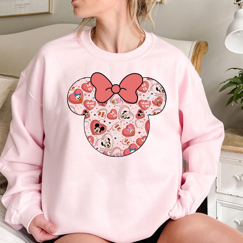 May include: Pink sweatshirt with a large graphic of Mickey Mouse ears with a bow. The ears are filled with a pattern of hearts, Mickey Mouse characters, and the words "Crazy 4 You" and "Love Ya".