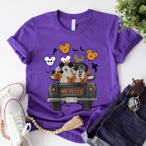 Peut inclure: T-shirt violet avec un motif sur le th&egrave;me d'Halloween repr&eacute;sentant Mickey et Minnie habill&eacute;s en fant&ocirc;mes dans un pick-up avec des citrouilles. Le texte "BOO TO YOU" est imprim&eacute; sur le camion.