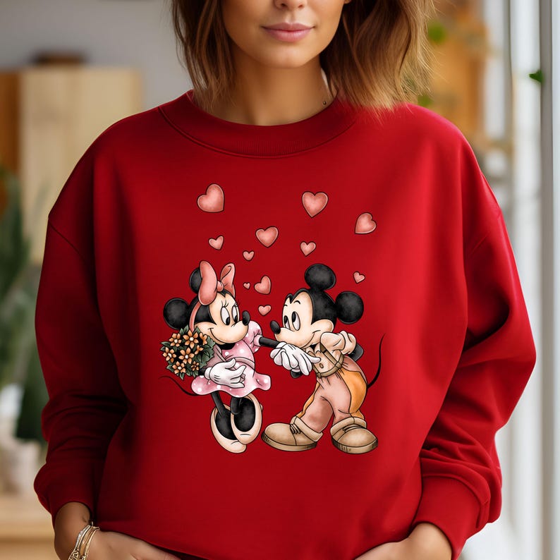 May include: Red sweatshirt with a graphic of Mickey Mouse and Minnie Mouse holding hands with hearts floating around them.