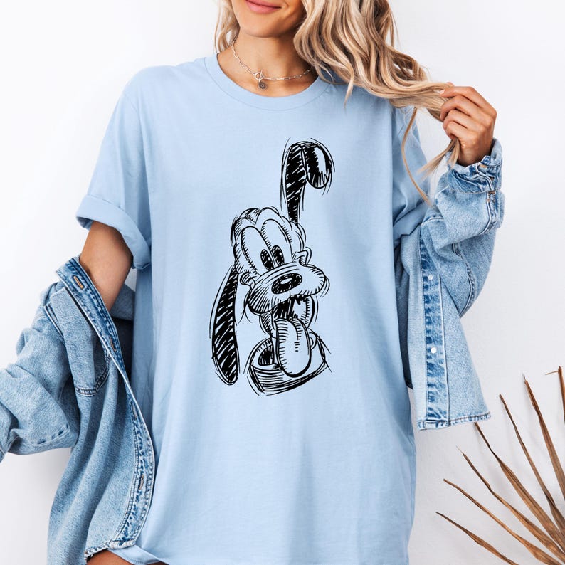 May include: Light blue long-sleeve t-shirt featuring a black and white sketch of a cartoon dog with its tongue out. The shirt has a relaxed fit and rolled-up sleeves. The dog illustration is centered on the front of the shirt.