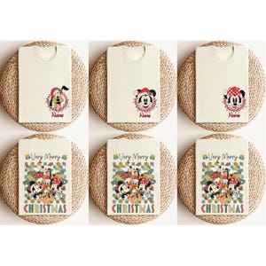 May include: Six cream-colored t-shirts with Christmas-themed designs. The shirts feature images of Disney characters like Pluto, Mickey, and Minnie Mouse, along with the text "Very Merry CHRISTMAS". Each shirt is folded and placed on a woven mat.