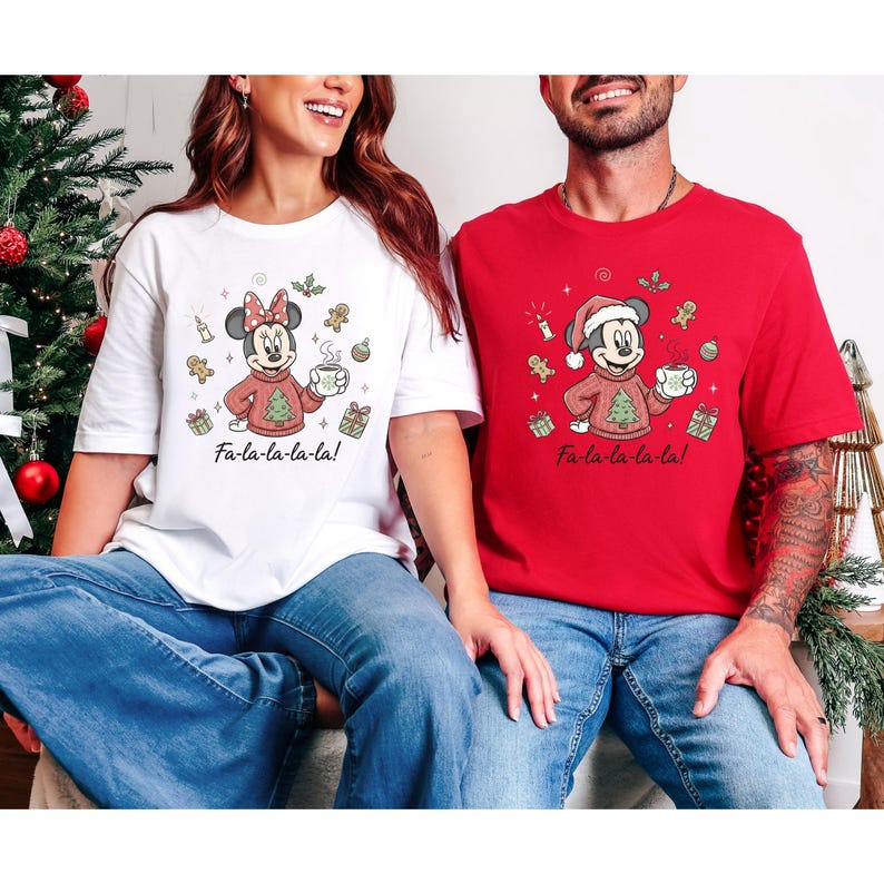May include: Two Christmas-themed t-shirts, one white and one red, featuring cartoon characters. The white shirt has Minnie Mouse in a red sweater, holding a mug, with the text "Fa-la-la-la-la!". The red shirt has Mickey Mouse in a Santa hat and sweater, also holding a mug, with the same text.