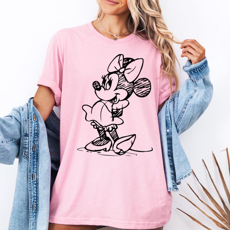 May include: A pink t-shirt with a black and white line drawing of Minnie Mouse on the front. Minnie Mouse is wearing a dress and has a bow in her hair.