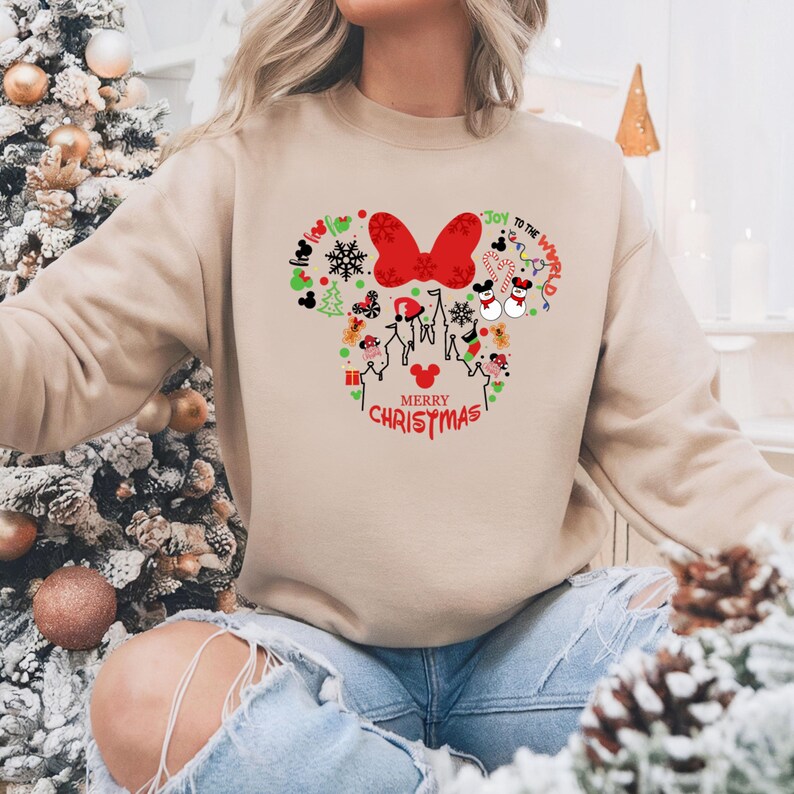 Pu&ograve; includere: Felpa beige con un design natalizio a forma di Minnie Mouse. Il design include un fiocco rosso, fiocchi di neve, teste di Topolino e il testo "Merry Christmas" e "Joy to the World."