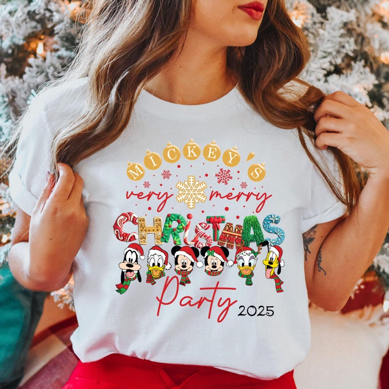 K&ouml;nnte beinhalten: Wei&szlig;es T-Shirt mit einem Weihnachtsmotiv mit Mickey Mouse und seinen Freunden. Der Text lautet "Mickey's Very Merry Christmas Party 2025".