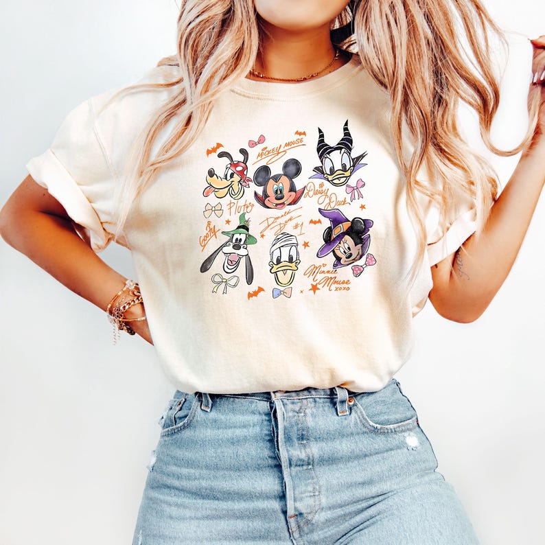 Puede incluir: Camiseta color crema con un gr&aacute;fico colorido de personajes de Disney con disfraces de Halloween. El gr&aacute;fico incluye Mickey Mouse, Minnie Mouse, Donald Duck, Daisy Duck, Goofy y Pluto. El texto incluye "Mickey Mouse", "Daisy Duck", "Donald Duck", "Minnie Mouse xoxo".
