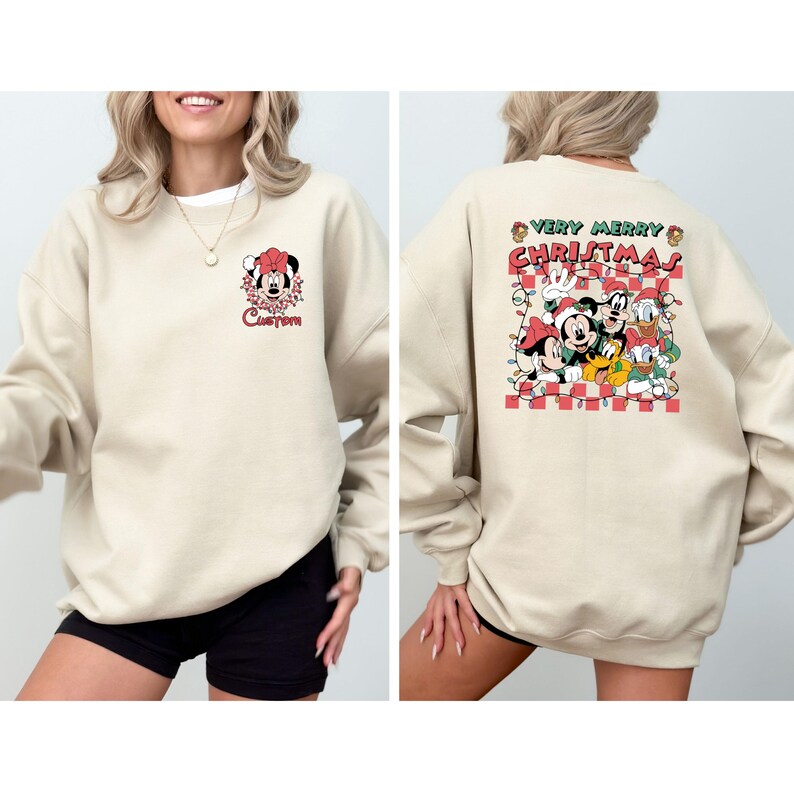 May include: A beige sweatshirt featuring a Christmas-themed design. The front displays a Minnie Mouse graphic with the word "Custom". The back showcases Mickey, Minnie, Donald, and Goofy with the text "Very Merry Christmas" on a red and white checkered background.