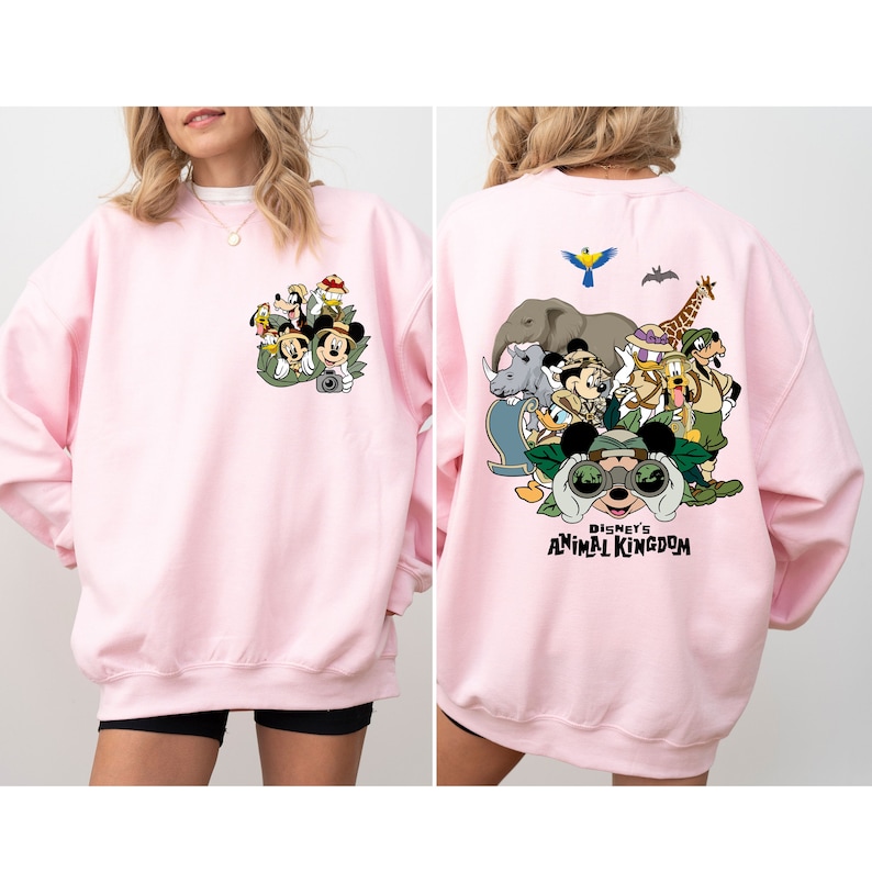 May include: Pink sweatshirt with a graphic print of Mickey Mouse and friends at Disney's Animal Kingdom. The print features Mickey Mouse, Donald Duck, Goofy, and other characters.