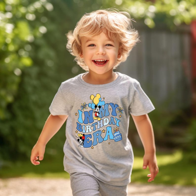 May include: A light gray t-shirt with a blue and yellow graphic that says "In My Birthday Era" with a cartoon Mickey Mouse character.