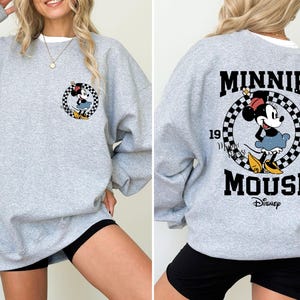 May include: Gray sweatshirt with a black and white checkered circle graphic featuring Minnie Mouse. The text "Minnie Mouse" and "Disney" are printed below the graphic.