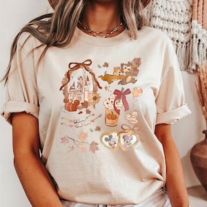 Puede incluir: Camiseta beige con un gr&aacute;fico tem&aacute;tico de oto&ntilde;o. El dise&ntilde;o incluye un castillo, calabazas, Chip y Chop, un caf&eacute; con leche de calabaza especiada y Mickey y Minnie Mouse en marcos en forma de coraz&oacute;n. La camiseta tiene mangas cortas.
