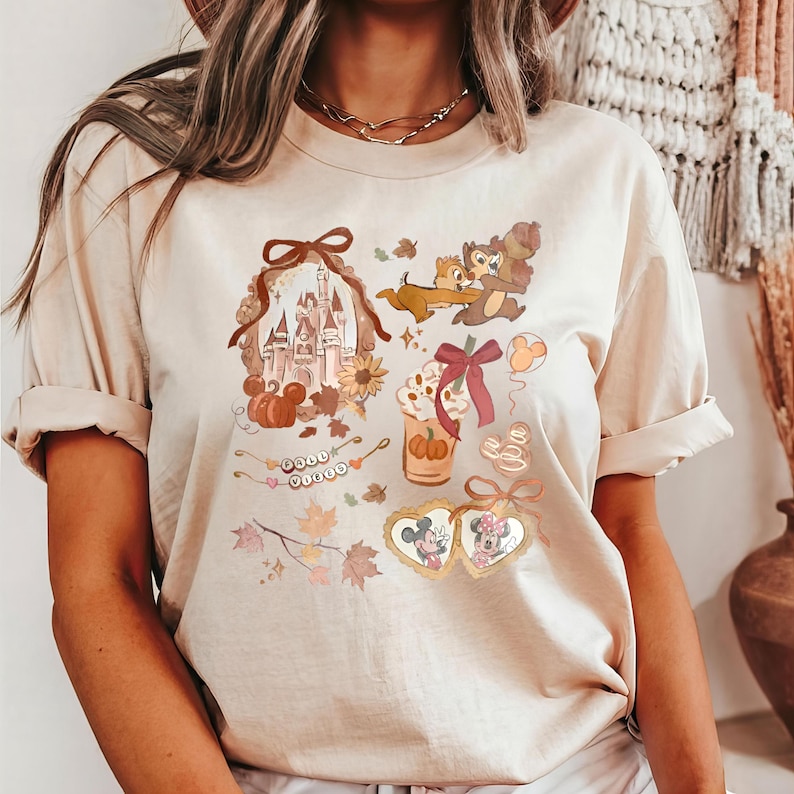 Puede incluir: Camiseta beige con un gr&aacute;fico tem&aacute;tico de oto&ntilde;o. El dise&ntilde;o incluye un castillo, calabazas, Chip y Chop, un caf&eacute; con leche de calabaza especiada y Mickey y Minnie Mouse en marcos en forma de coraz&oacute;n. La camiseta tiene mangas cortas.
