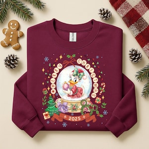 Pode incluir: Camisola bord&ocirc; com um design de globo de neve com a Margarida segurando um enfeite rosa. As palavras "Merry Christmas" e o ano "2025" s&atilde;o exibidos. Roupas festivas de Natal.