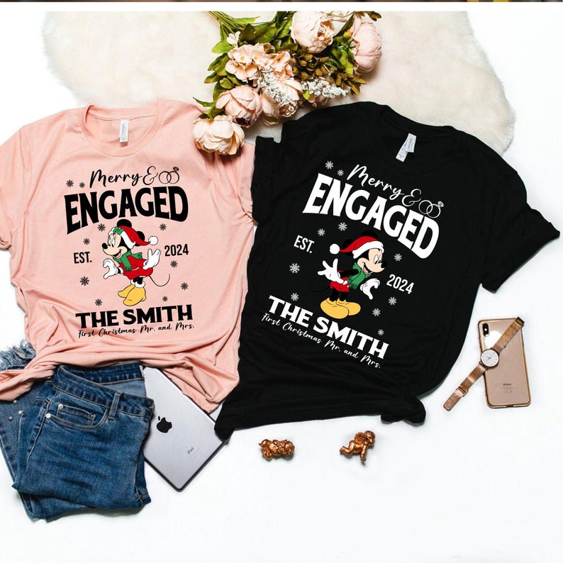 Puede incluir: Dos camisetas rosas y negras con un personaje de Mickey Mouse con un gorro de Pap&aacute; Noel. Las camisetas dicen "Merry & Engaged" con el a&ntilde;o 2024 y "The Smith" con el texto "First Christmas Mr. and Mrs."