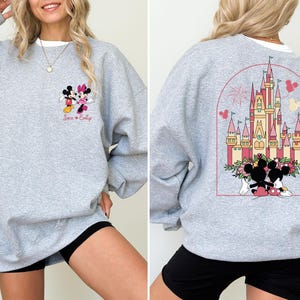 K&ouml;nnte beinhalten: Grauer Pullover mit einem Mickey Mouse und Minnie Mouse Motiv auf der Vorderseite und einem Motiv von Schloss Aschenputtel mit Mickey Mouse und Minnie Mouse auf der R&uuml;ckseite. Der Text "Jack & Emily" ist unter dem Mickey Mouse und Minnie Mouse Motiv gedruckt.
