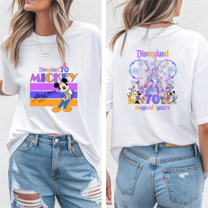 May include: White t-shirt with a graphic of Mickey Mouse and the text "Disneyland 70 Mickey" on the front. The back of the shirt features a graphic of the Disneyland castle with fireworks and the text "Disneyland 70 magical years".