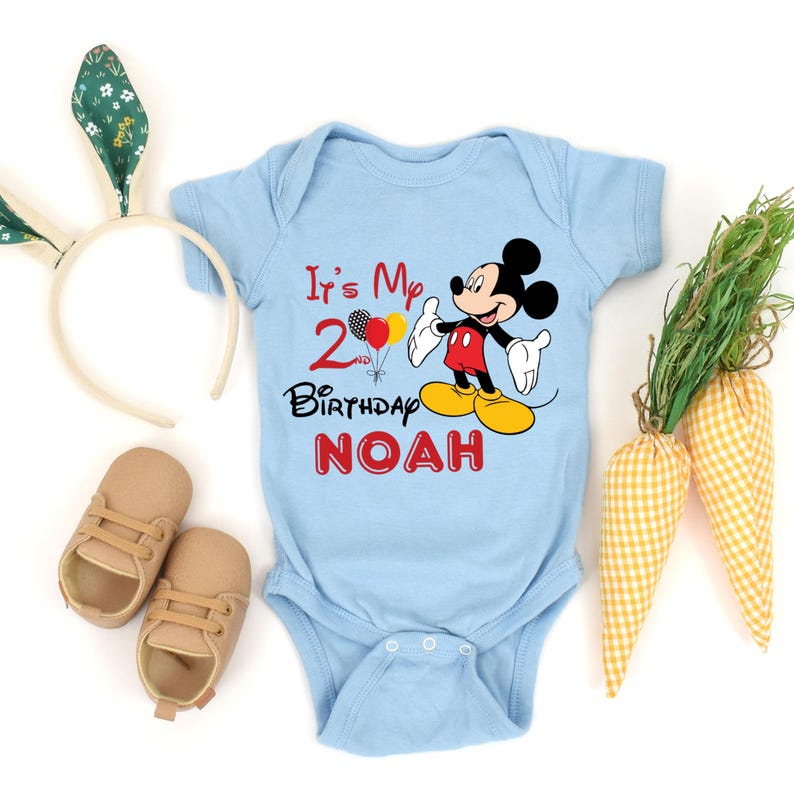 May include: A light blue baby onesie with a Mickey Mouse graphic and the text "It's My 2nd Birthday NOAH".