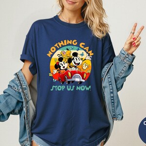 May include: Navy blue t-shirt featuring a colorful graphic of Mickey and Minnie Mouse in a red car, with the text "NOTHING CAN STOP US NOW!". The design includes butterflies and a yellow sun. The shirt is a Comfort Colors brand.