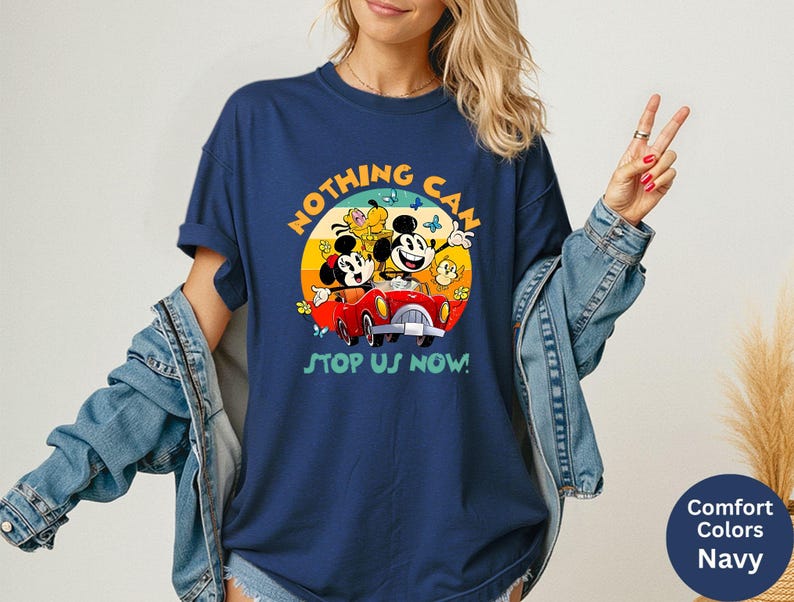 May include: Navy blue t-shirt featuring a colorful graphic of Mickey and Minnie Mouse in a red car, with the text "NOTHING CAN STOP US NOW!". The design includes butterflies and a yellow sun. The shirt is a Comfort Colors brand.