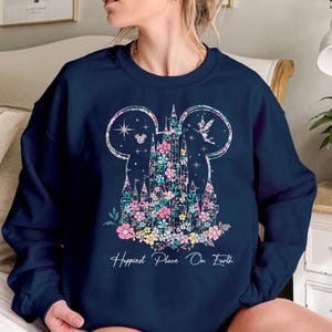May include: A navy blue sweatshirt with a floral design of a castle and Mickey Mouse ears. The text "Happiest Place On Earth" is printed below the design.