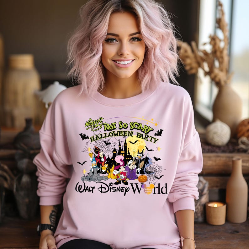 May include: Pink sweatshirt with a graphic of Mickey Mouse and friends in Halloween costumes. The text on the shirt reads "Mickey's Not So Scary Halloween Party Walt Disney World".