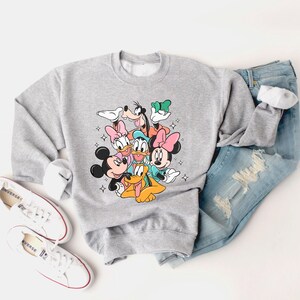 May include: A gray sweatshirt with a graphic print of Mickey Mouse, Minnie Mouse, Donald Duck, Goofy, Pluto, and Daisy Duck. The characters are all smiling and appear to be hugging each other.