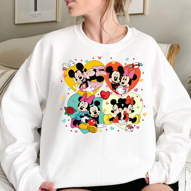 May include: White sweatshirt with a colorful graphic print of Mickey Mouse and Minnie Mouse in various poses. The graphic features hearts, stars, and other decorative elements.