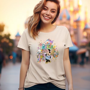May include: A beige t-shirt with a colorful graphic of Mickey Mouse in front of the Epcot logo and a roller coaster. The graphic also includes flowers, stars, and a dragon.