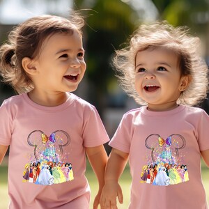 Puede incluir: Dos ni&ntilde;as peque&ntilde;as con camisetas rosas con un gr&aacute;fico de princesas Disney y el castillo de Cenicienta. Las camisetas tienen un dise&ntilde;o de orejas de Mickey con un lazo.