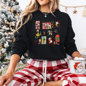 May include: Black sweatshirt with a festive Christmas design featuring cartoon characters and the text "Merry Christmas." The design includes images of Mickey Mouse, Minnie Mouse, Donald Duck, and other holiday elements. The person is wearing red and white plaid pajama pants.