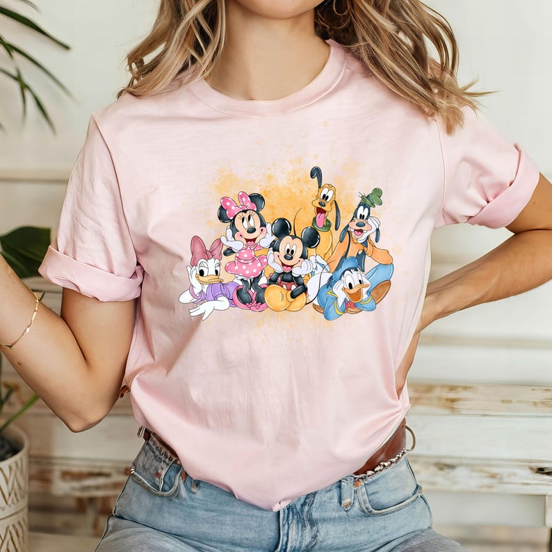 Puede incluir: Una camiseta rosa con un estampado gr&aacute;fico de Mickey Mouse, Minnie Mouse, Donald Duck, Goofy y Pluto. Los personajes est&aacute;n todos sonriendo y parecen estar divirti&eacute;ndose juntos.