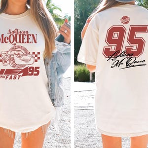 May include: White t-shirt with a red graphic of Lightning McQueen from Cars. The graphic includes the text "Lightning McQueen", "Think Fast", and the number "95". The back of the shirt has a red number "95" with the text "Lightning McQueen" in a cursive font.