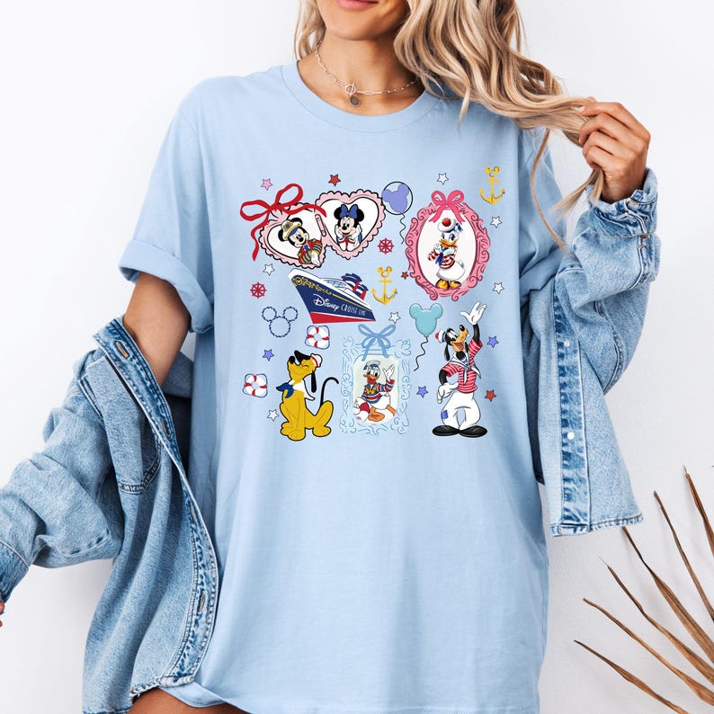Puede incluir: Camiseta azul claro con un estampado gr&aacute;fico colorido con Mickey Mouse, Minnie Mouse, Donald Duck, Goofy y Pluto. El gr&aacute;fico incluye un crucero, corazones, estrellas y anclas. El texto "Disney Cruise Line" es visible en el barco.