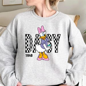 May include: Gray sweatshirt with a checkered black and white graphic of Daisy Duck with the word "DAISY" in the graphic and the number "1940" below the graphic.