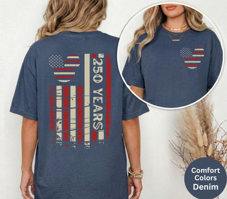 May include: A denim blue t-shirt with a distressed American flag design on the back, featuring a Mickey Mouse head shape and the text "250 YEARS". A smaller version of the flag design is on the front pocket.
