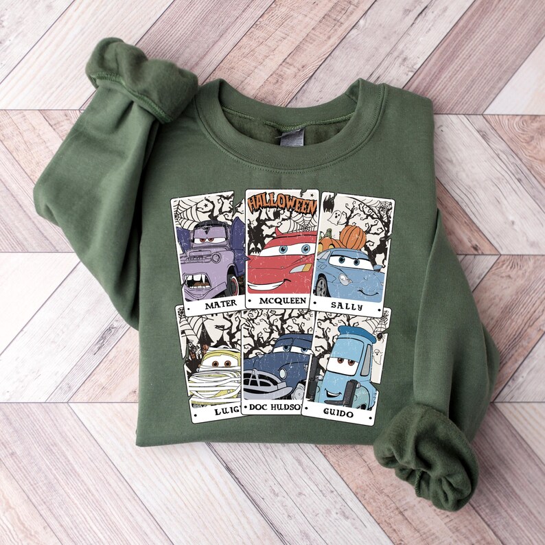 May include: Green sweatshirt with a graphic print of the Cars characters dressed up for Halloween. The characters are Mater, McQueen, Sally, Luigi, Doc Hudson, and Guido. The text "HALLOWEEN" is printed above the characters.